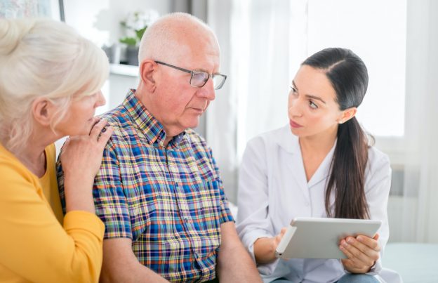 Nurse gives bad news to worried senior couple at home